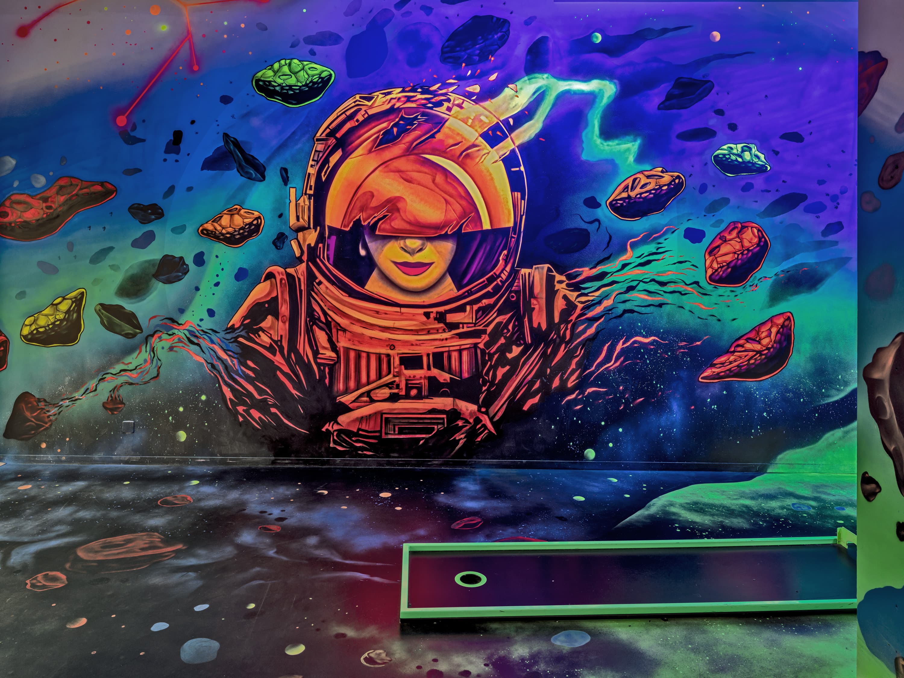 Leuchtendes Schwarzlicht-Wandbild mit einer Astronautin zwischen Asteroiden über einer Minigolfbahn bei Galaxy Golf Zürich.
