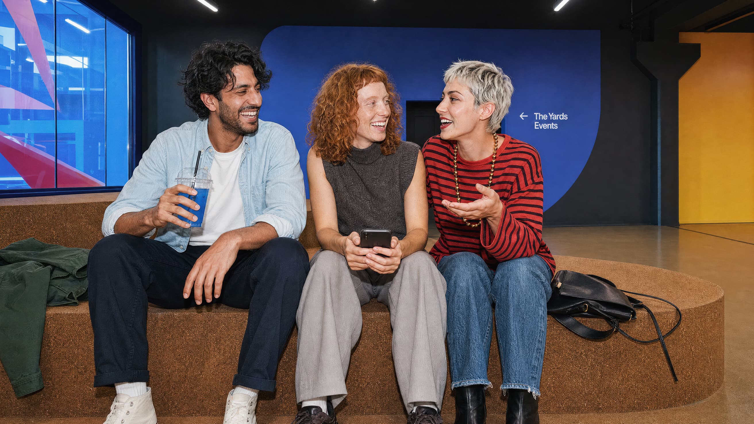 Drei junge Erwachsene sitzen auf Lounge vor The Yards Events Aufgang.